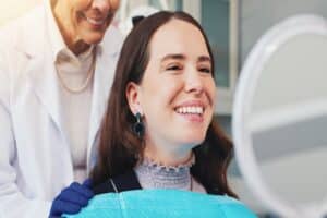 Woman smiling in mirror during dental visit for cleaning, tooth whitening, and veneer inspection, concept of oral hygiene and dental care